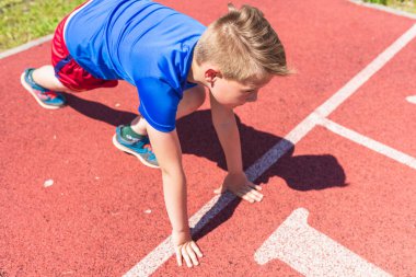 Kafkasyalı okul çocuğu kırmızı pistte koşmaya hazır ol. Başlangıç pozisyonunda koşmaya hazır genç çocuk. Sağlıklı bir yaşam tarzı..