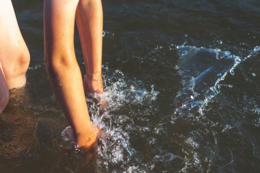 Küçük çocuk suda oynuyor ve gölde ya da nehirde hazırlanması ve damlalarla eğlenmesi için sükse yaptırıyor..