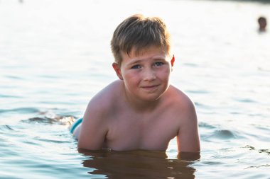 Tatlı genç çocuk sıcak günbatımında ya da gölde ya da plaj suyunda eğlenmeyi sever. Mutlu çocukluk tatili taşra konseptinde. Çocuk iskelede sıcak bir yaz gününde suda iyi vakit geçiriyor..