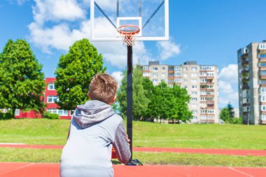 Çocuk oyun sahasında basketbol atışına hazırlanıyor. Çocuk güneşli yaz günlerinde oyun sahasında basket oynuyor..