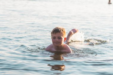 Mutlu gülümseyen çocuk suda yüzerken eğleniyor. Tatlı çocuk suda yüzüyor. Çocuk sahilde eğleniyor. Yaz tatili. Aktif yaşam tarzı konsepti. Yaz tatilindeki mutlu çocuk..