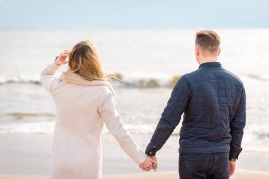 Genç aşık çift, çekici erkek ve kadın sahilde romantik bir akşam geçiriyorlar, el ele tutuşup gün batımını izliyorlar.