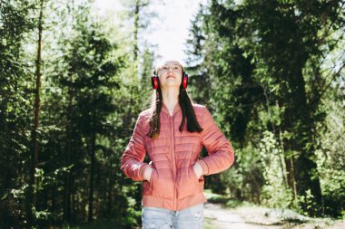 Sevimli, neşeli, sıska bir genç kız ormanda müzik dinlerken yaz, bahar ormanı ya da park manzarası seyrediyor. Yaklaş..