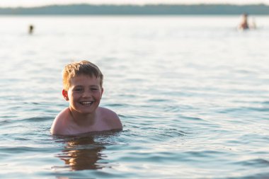Tatlı genç çocuk sıcak günbatımında ya da gölde ya da plaj suyunda eğlenmeyi sever. Mutlu çocukluk tatili taşra konseptinde. Çocuk iskelede sıcak bir yaz gününde suda iyi vakit geçiriyor..