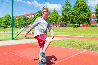 Basketbolcu çocuk sahada esneme hareketleri yapıyor. Çocuk ısınıyor. Güneşli bir günde Red Court Sokağı 'nda..