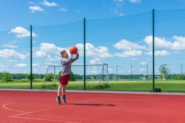 Çekici genç çocuk oyun sahasında potaya top atıyor. Tatlı çocuk yaz aylarında oyun bahçesinde basketbol oynuyor..