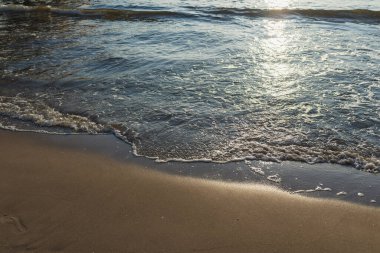 Kumlu akşam kumsalında denizin yumuşak dalgası. Odaklanma, bulanık görüntü. Boşluğu kopyala.