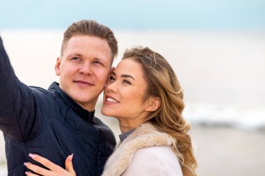 Güzel, genç, mutlu bir kadın güneşli sahilde fotoğraf çekerken sarılıyor, genç erkek arkadaşına sarılıyor. Yakından..