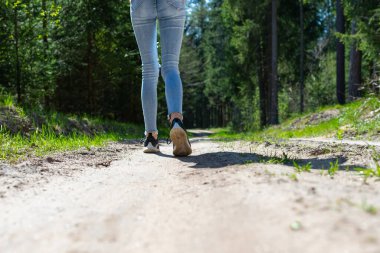 Kadın turist bacakları ve spor ayakkabıları orman yolunda yürüyor. Gün ışığı..
