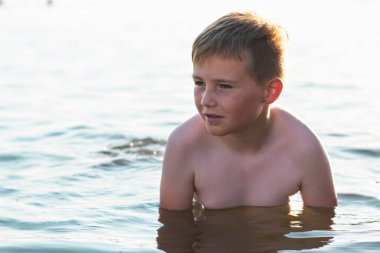 Tatlı genç çocuk sıcak günbatımında ya da gölde ya da plaj suyunda eğlenmeyi sever. Mutlu çocukluk tatili taşra konseptinde. Çocuk iskelede sıcak bir yaz gününde suda iyi vakit geçiriyor..