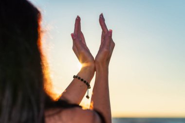 Güzel bir yaz güneşi gündönümü konsepti. Genç kadın ellerinin silueti rahatlatıcı, mutlu meditasyon yapıyor ve kumsalda altın saat gökyüzüne karşı gün batımını tutuyor..