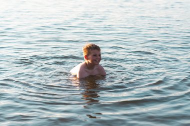 Tatlı genç çocuk sıcak günbatımında ya da gölde ya da plaj suyunda eğlenmeyi sever. Mutlu çocukluk tatili taşra konseptinde. Çocuk iskelede sıcak bir yaz gününde suda iyi vakit geçiriyor..