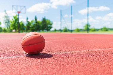 Kırmızı kauçuk bir sahada turuncu eski basketbol topu. Güneşli yaz sıcağı. Arka plan bulanık. Turuncu top oyuncuyu bekliyor..