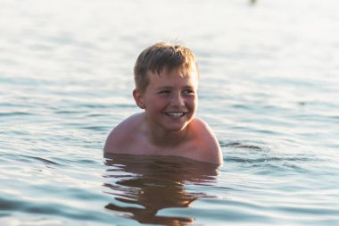 Tatlı genç çocuk sıcak günbatımında ya da gölde ya da plaj suyunda eğlenmeyi sever. Mutlu çocukluk tatili taşra konseptinde. Çocuk iskelede sıcak bir yaz gününde suda iyi vakit geçiriyor..