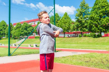 Basketbolcu çocuk sahada esneme hareketleri yapıyor. Çocuk ısınıyor. Güneşli bir günde Red Court Sokağı 'nda..