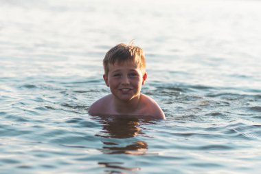 Tatlı genç çocuk sıcak günbatımında ya da gölde ya da plaj suyunda eğlenmeyi sever. Mutlu çocukluk tatili taşra konseptinde. Çocuk iskelede sıcak bir yaz gününde suda iyi vakit geçiriyor..