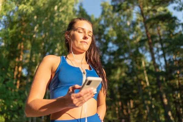 Young pretty woman at outdoors listening music with a mobile in a summer park.Cute female listening to music during training at park. Copy space