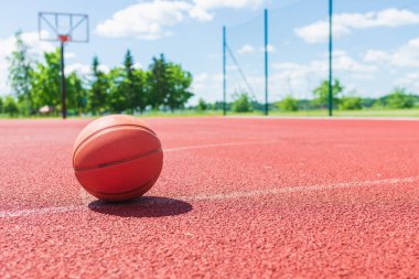 Kırmızı kauçuk bir sahada turuncu eski basketbol topu. Güneşli yaz sıcağı. Arka plan bulanık. Turuncu top oyuncuyu bekliyor..