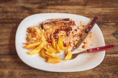 Partiden sonra yemek artıkları yerinde. Kapalı çatal, tabakta bıçak, ahşap masada yemekten sonra boş..
