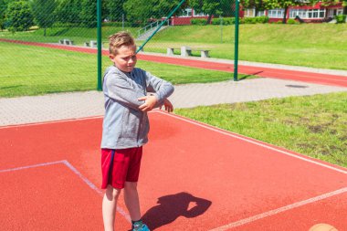 Basketbolcu çocuk sahada esneme hareketleri yapıyor. Çocuk ısınıyor. Güneşli bir günde Red Court Sokağı 'nda..
