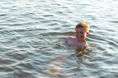 Mutlu gülümseyen çocuk suda yüzerken eğleniyor. Tatlı çocuk suda yüzüyor. Çocuk sahilde eğleniyor. Yaz tatili. Aktif yaşam tarzı konsepti. Yaz tatilindeki mutlu çocuk..