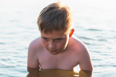 Tatlı genç çocuk sıcak günbatımında ya da gölde ya da plaj suyunda eğlenmeyi sever. Mutlu çocukluk tatili taşra konseptinde. Çocuk iskelede sıcak bir yaz gününde suda iyi vakit geçiriyor..