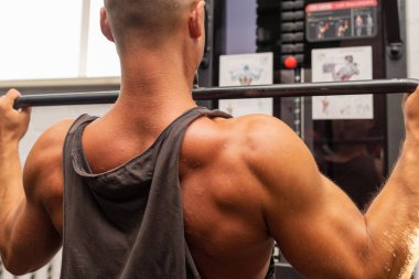 Spor salonunda egzersiz yapan kaslı bir adam, spor salonunda triseps egzersizi yapan. Güçlü çıplak erkek karın kası. Yakışıklı vücut geliştirici. Spor salonunda kapalı alanda çalışıyor..