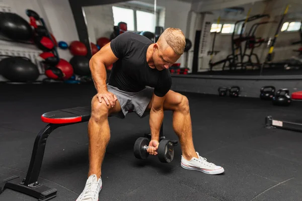 Young athlete Working out biceps at the gym. muscular young man lifting weights in gym on a dark background.Closeup.Wide view.