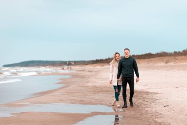 Attractive young couple walking along the shore of a sandy beach, on a spring romantic holiday, outdoors. Travel tourists lifestyle. Couple enjoying loving time together.Copy space.