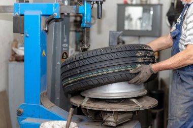 Tamirci araba servisinde lastik değiştiriyor. Lastik döndürme makinesi. Araba tamircisi atölyede tekerlek takar. Atölyedeki lastik kurulumu, yakın plan..