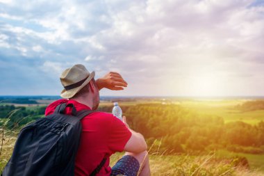 Sırt çantalı bir adam terini silip dağ ormanında su şişesini tutuyor. Yaz seyahati konsepti.
