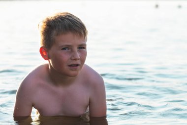 Tatlı genç çocuk sıcak günbatımında ya da gölde ya da plaj suyunda eğlenmeyi sever. Mutlu çocukluk tatili taşra konseptinde. Çocuk iskelede sıcak bir yaz gününde suda iyi vakit geçiriyor..