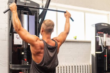 Spor salonunda egzersiz yapan kaslı bir adam, spor salonunda triseps egzersizi yapan. Güçlü çıplak erkek karın kası. Yakışıklı vücut geliştirici. Spor salonunda kapalı alanda çalışıyor..