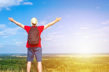 Sırt çantalı turist. Sırt çantalı, kollarını açmış gezgin. Mavi gökyüzü beyaz bulutlu yaz manzarasında duruyor.