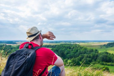 Sırt çantalı bir adam terini silip dağ ormanında su şişesini tutuyor. Yaz seyahati konsepti.
