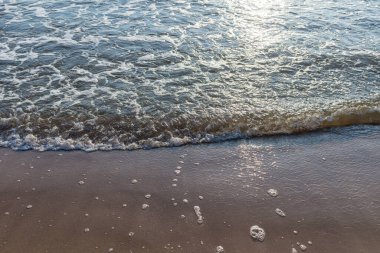 Kumlu akşam kumsalında denizin yumuşak dalgası. Odaklanma, bulanık görüntü. Boşluğu kopyala.