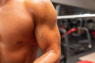 Koyu renk spor arka planında oturan kaslı, terli genç adamın terli vücudu. Ter birikintisini kapat. vücut sıkı çalışmadan sonra.