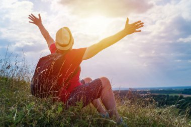 Sırt çantalı turist. Sırt çantalı, kollarını açmış gezgin. Mavi gökyüzü beyaz bulutlu yaz manzarasında duruyor.