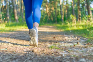Athletic pair of legs running or jogging on a path during sunrise or sunset.healthy lifestyle concept. young fitness woman legs walking on summer forest trail.Back view,closeup.