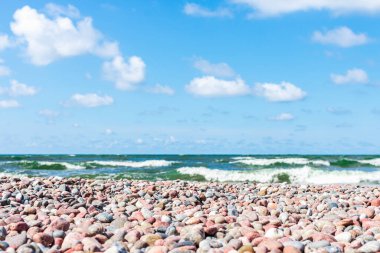 Kıyıda küçük çakıl taşları. Güneşli yaz günü mavi gökyüzü, beyaz bulutlar. Güzel, yalnız, küçük çakıl taşı plajı. Uzayı kopyala..