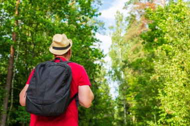 Gezgin genç adam yaz ormanlarında yolda yürüyor. Sırt çantalı genç adam sıcak yaz gününde tek başına ormanı geziyor. Turizm ve aktif yaşam tarzı kavramı..