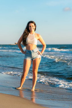 Gün batımında, deniz sahilinde, günlük giysiler içinde güzel seksi bir kız kameraya bakar. Havalı bir kızın yakın çekimi. Açık hava modelinin güzel bir portresi..