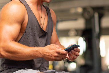 Spor salonunda kulaklıklı akıllı telefon kullanan bir adam kulaklıklı bir sporcu akıllı telefonundan müzik seçiyor ve spor salonunda egzersiz yapmaya hazırlanıyor. Modern teknolojiler, sağlıklı yaşam tarzı kavramı. Boşluğu kopyala.