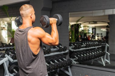 Güçlü vücut geliştirici, spor salonunda dambılla egzersiz yapıyor. Genç, yakışıklı, yetişkin bir erkek, modern spor salonunda tek kollu halterde kürek çekiyor. Boşluğu kopyala..