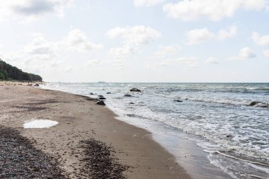 Birkaç turist ile boş kumlu güzel bir sahil. Mavi gökyüzü, beyaz bulutlar, yaz günü..