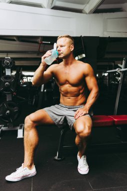 Genç beyaz adam egzersiz yaptıktan sonra su içiyor. Salonda sallantıdan su içen adam. Egzersiz sonrası dinlenen ve Shaker 'dan içen kaslı adam..