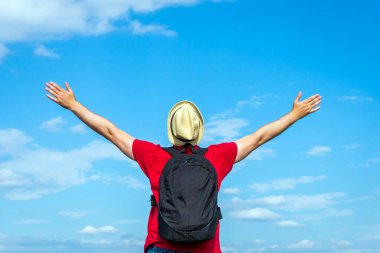 Sırt çantalı turist. Sırt çantalı, kollarını açmış gezgin. Mavi gökyüzü beyaz bulutlu yaz manzarasında duruyor.