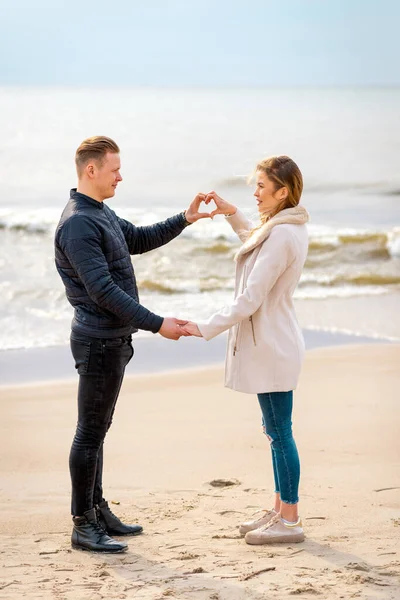 ロマンチックな若いカップルは ビーチに立っている間にお互いを見て笑顔で 心を作っています — ストック写真