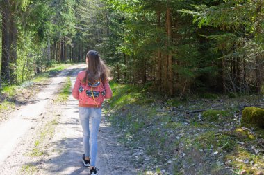 Sırt çantalı genç bir kız turist yaz günü ormanda yürüyor. Hipster yaşam tarzı ve tek kişilik gezi..