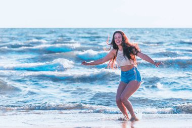 Yazın denizde oynayan genç bir kadın. Kadınlar deniz suyuyla su sıçratır. Sahilde eğlenen neşeli genç bir kadın. Deniz suyuna su sıçratıyor ve tatilin tadını çıkarıyor..